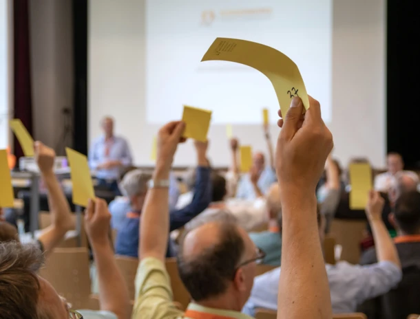 Vertreter:innen unserer Energiegenossenschaften halten bei der Bürgerwerke-Generalversammlung Stimmzettel in die Höhe..